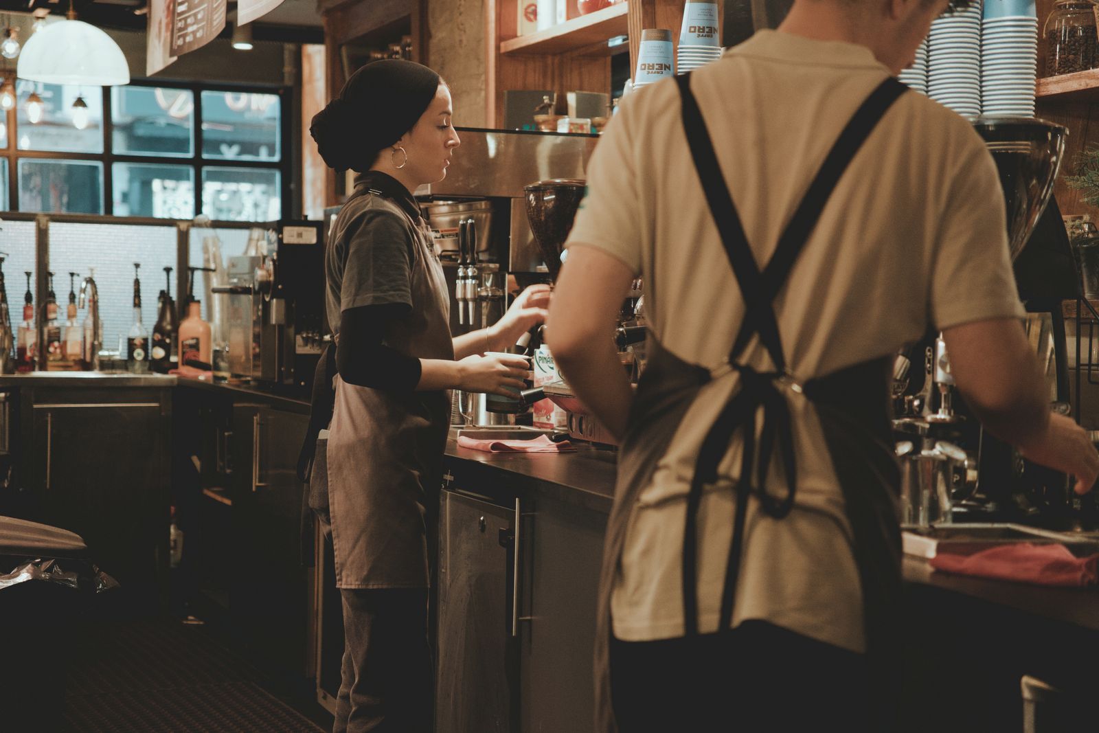 Two baristas at work behind the bar at Almanac, warm light on the espresso machine