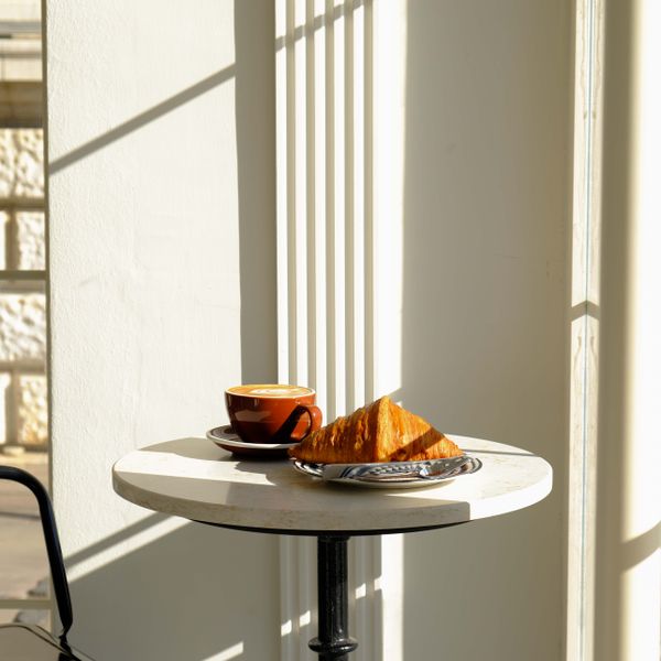 A small table by the window with a croissant in the sun