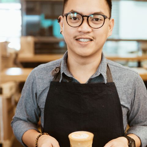 Theo, in an apron, holding a cappuccino