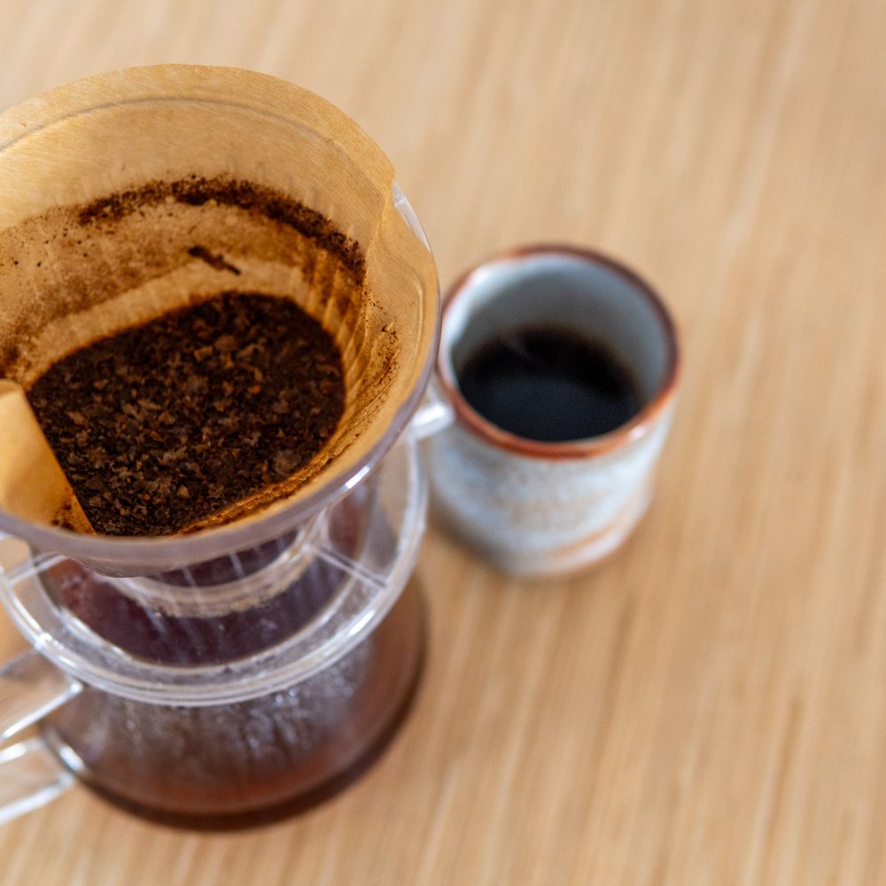 A pour-over dripper next to a cup of coffee, seen from above