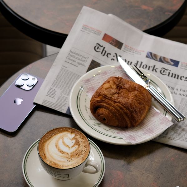 A newspaper, a pastry and a flat white on a dark table